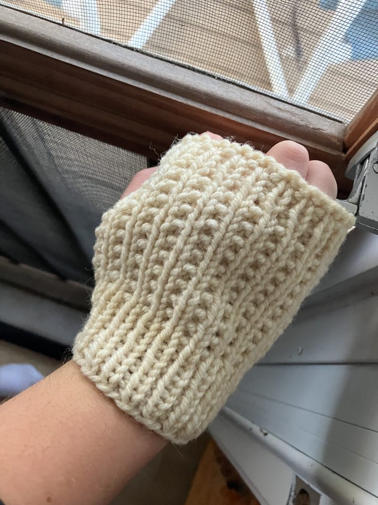 Hand with seed and furrow fingerless mitt holding onto screen door handle.